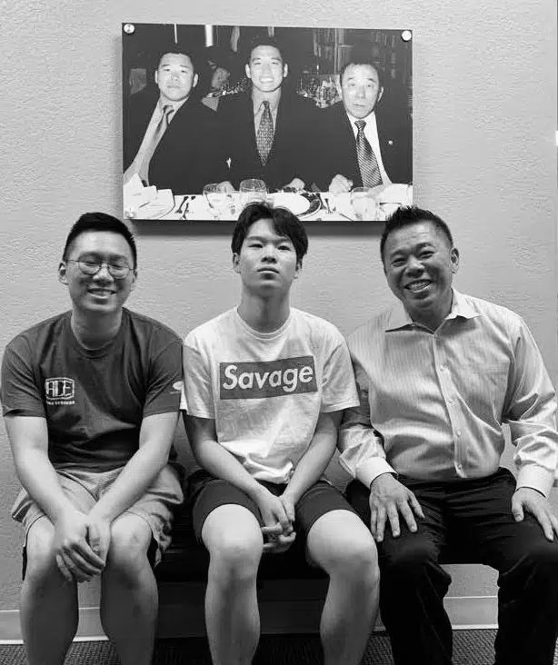 Kwan smiling with two young men in front of a framed black and white photo of a past event.